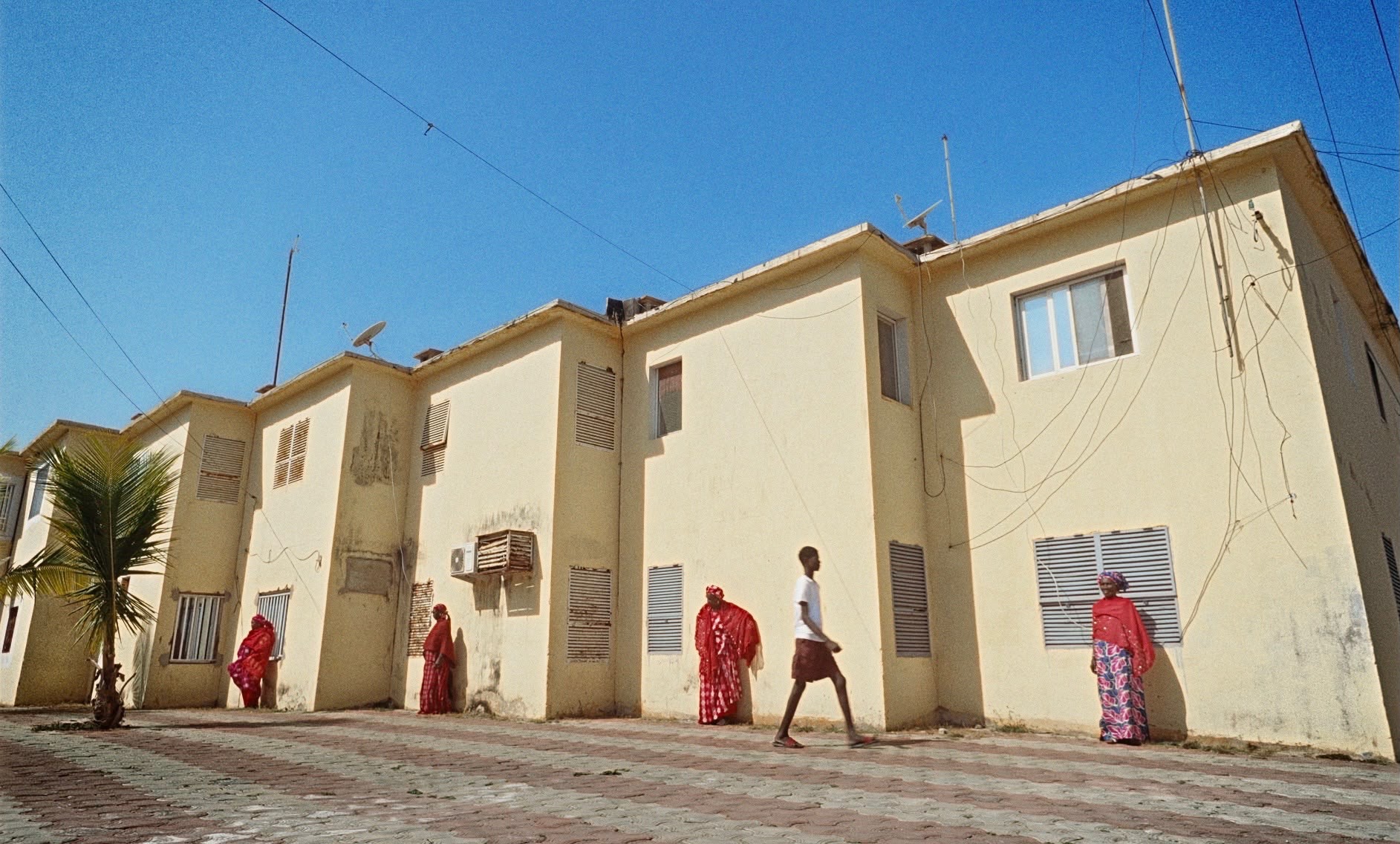 People walking beside sunlit buildings, with figures dressed in vibrant red